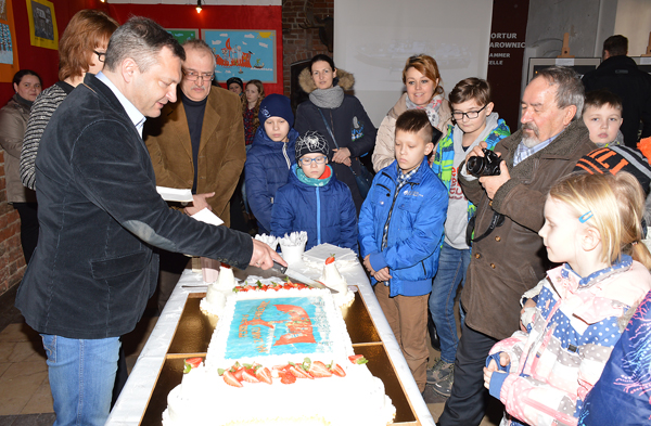 Zdjęcie z&nbsp;wernisażu ferii na zamku w&nbsp;Darłowie. Starosta sławieński częstuje tortem uczestników warsztztów.